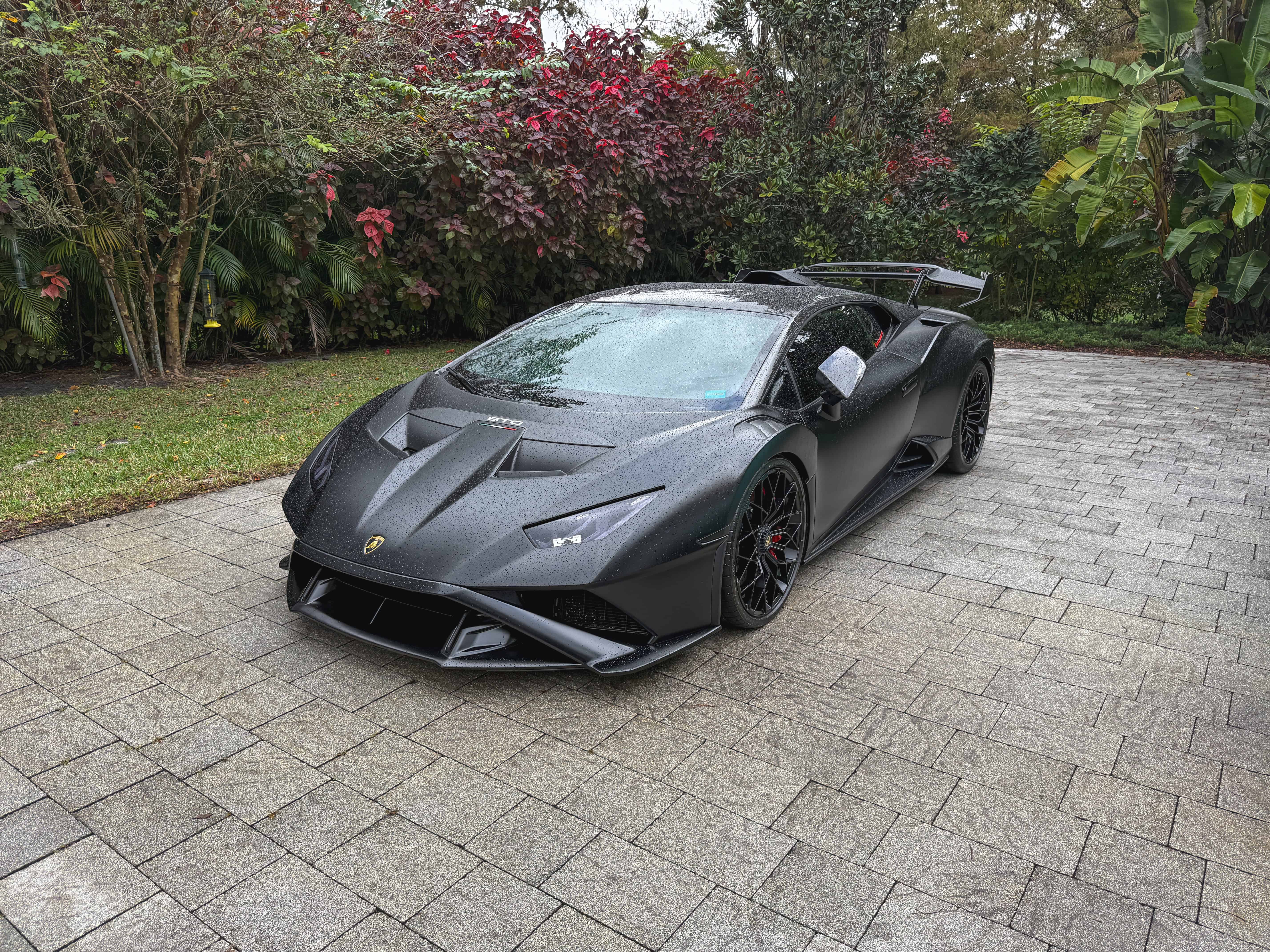 High-quality matte black Lamborghini with rain droplets on sleek exterior.